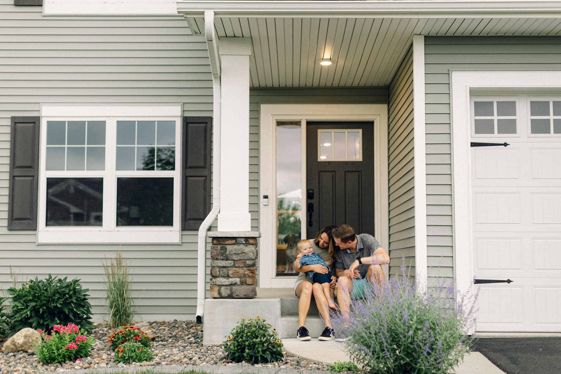 Parents and young son sitting together on the front steps of their home