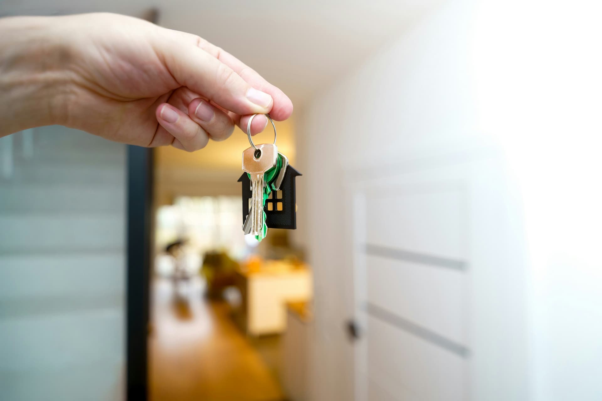 Hand holding house keys with a house keychain inside a new home