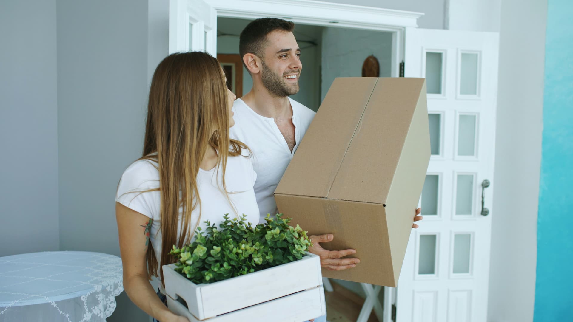 Smiling young couple carrying a moving box and plants into their new home