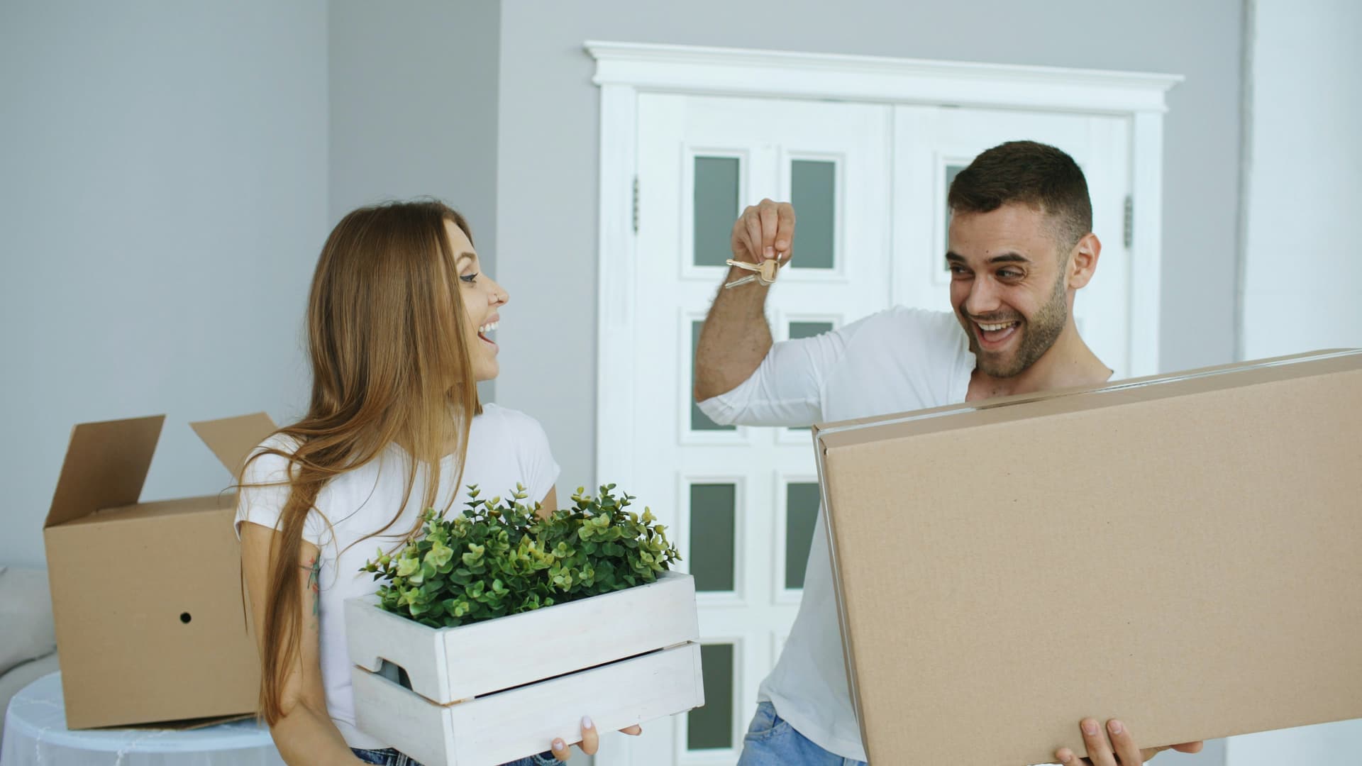 Excited couple holding up the keys to their new home while carrying moving boxes