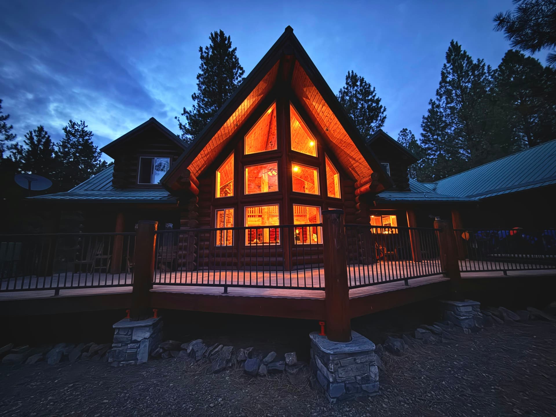 Timber-frame mountain home with a tall glass gable glowing at dusk among pines