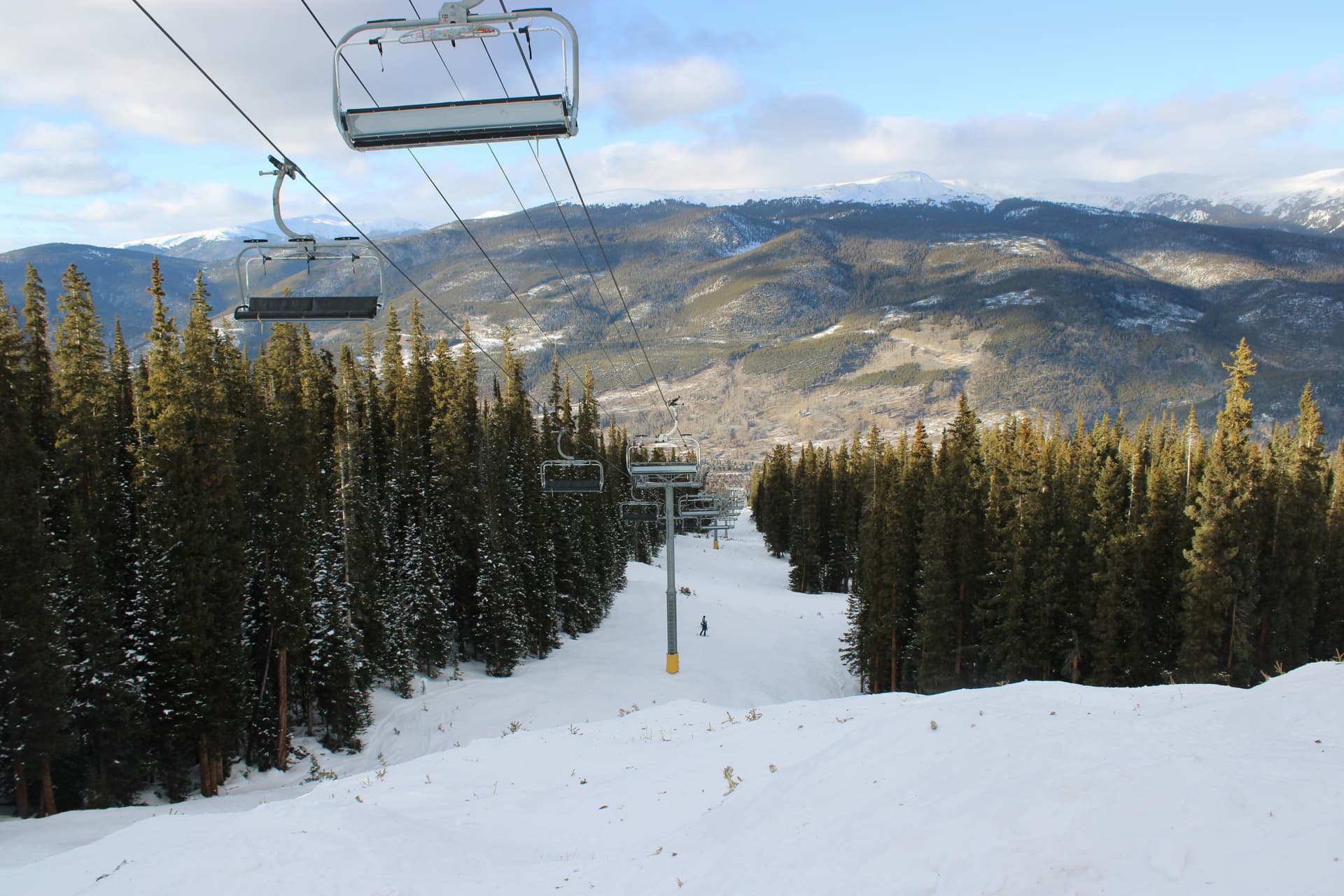 Chairlift climbing a groomed run through pines at Keystone
