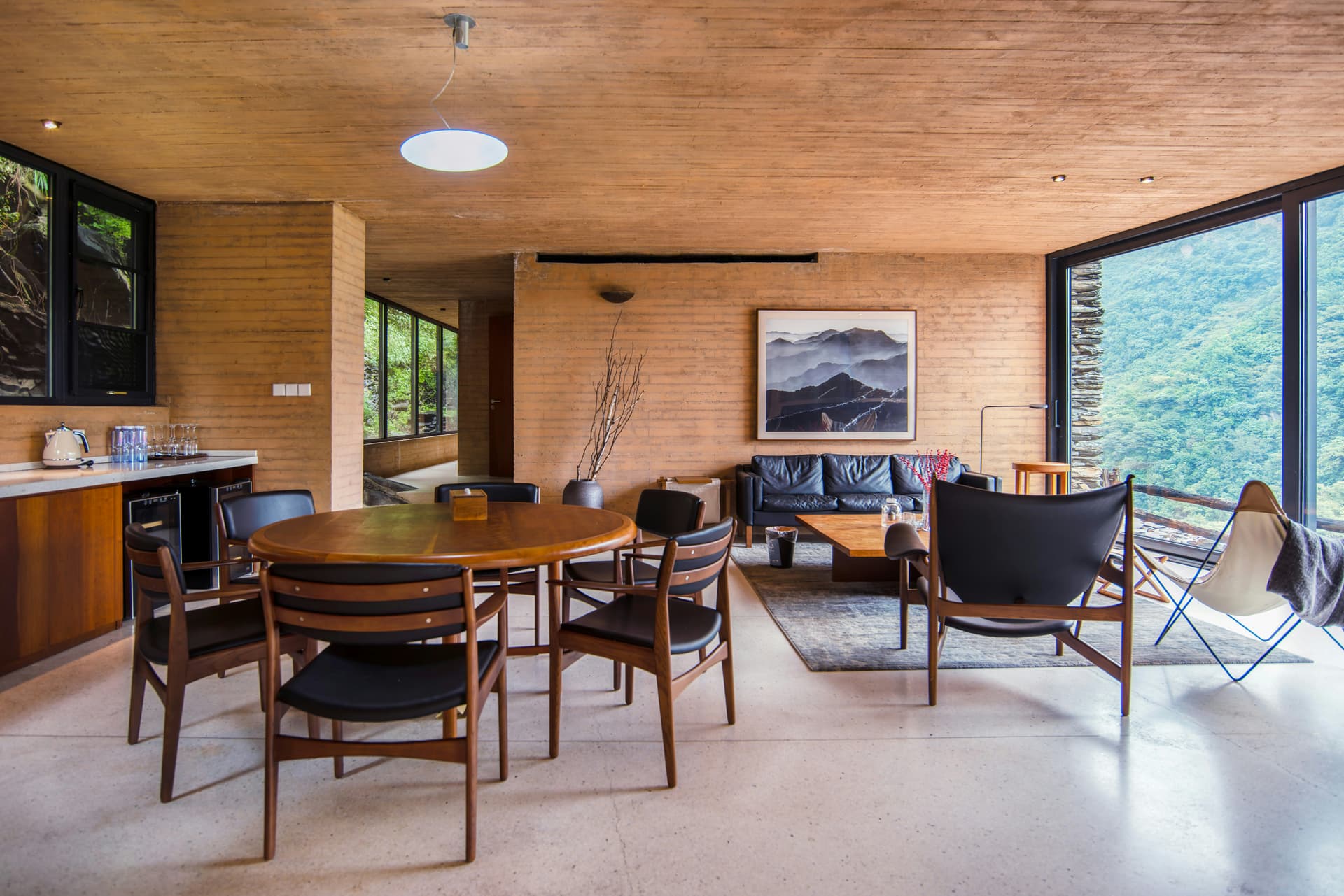 Bright wood-paneled living and dining room with a wall of glass onto forested mountains